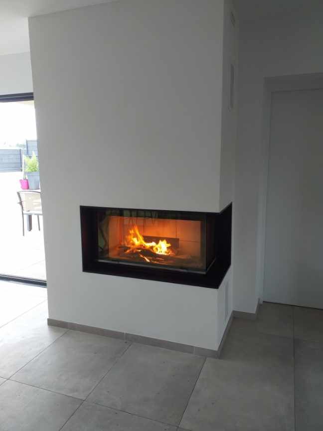 Cheminée blanche moderne avec un feu qui brûle à l'intérieur, sur un sol carrelé gris, à côté d'un mur blanc.