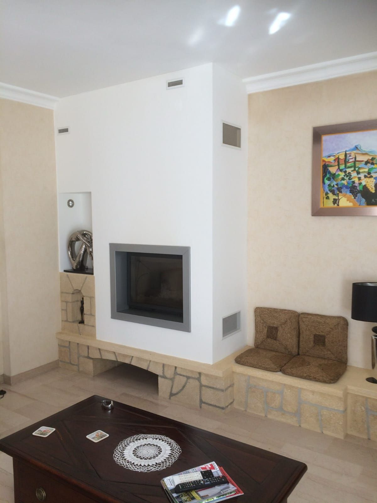 Une cheminée blanche moderne dans une pièce aux murs beige clair et avec un banc bas en briques.