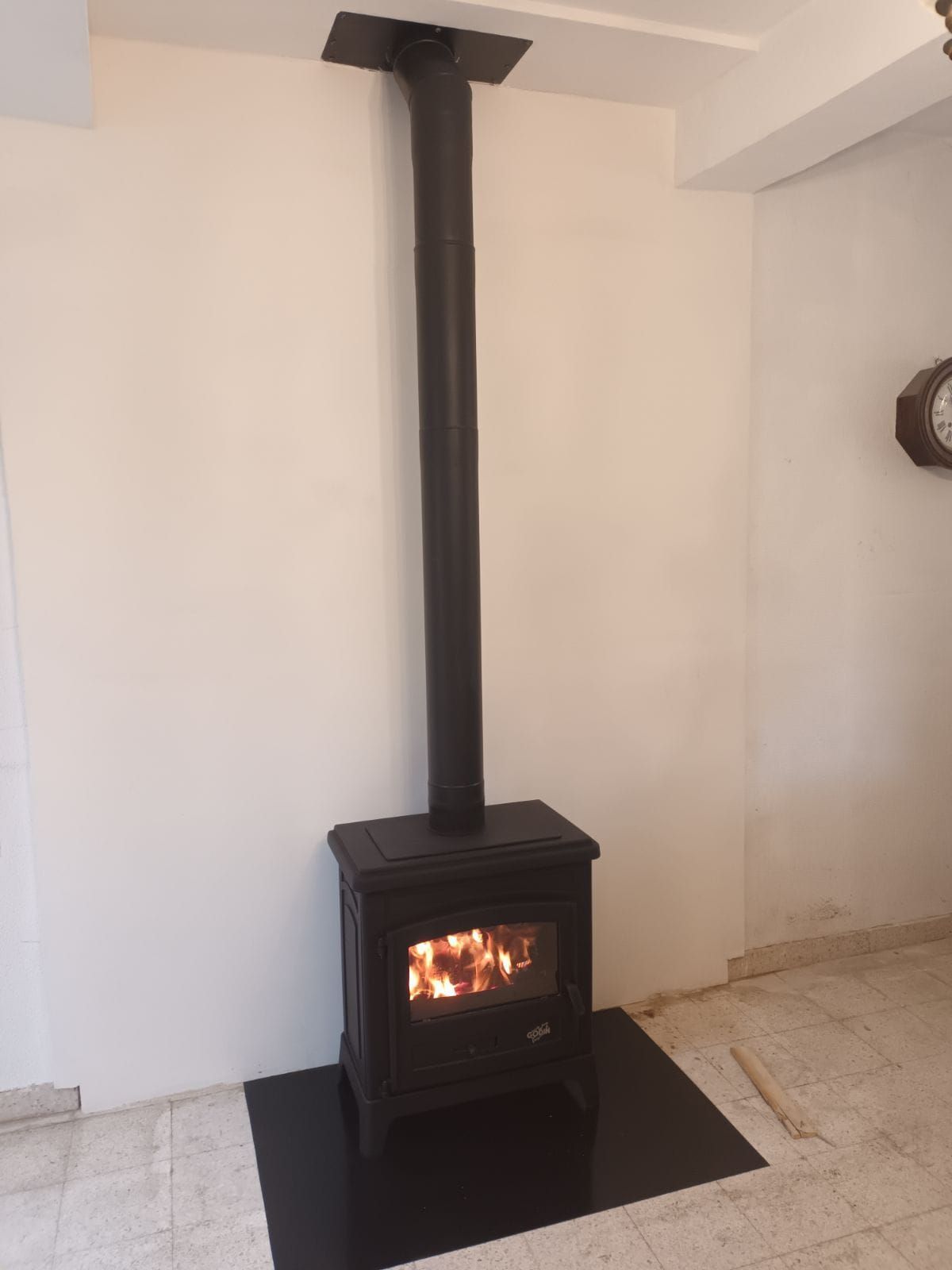Poêle à bois noir avec un feu allumé, une cheminée noire et un foyer sur un mur blanc.