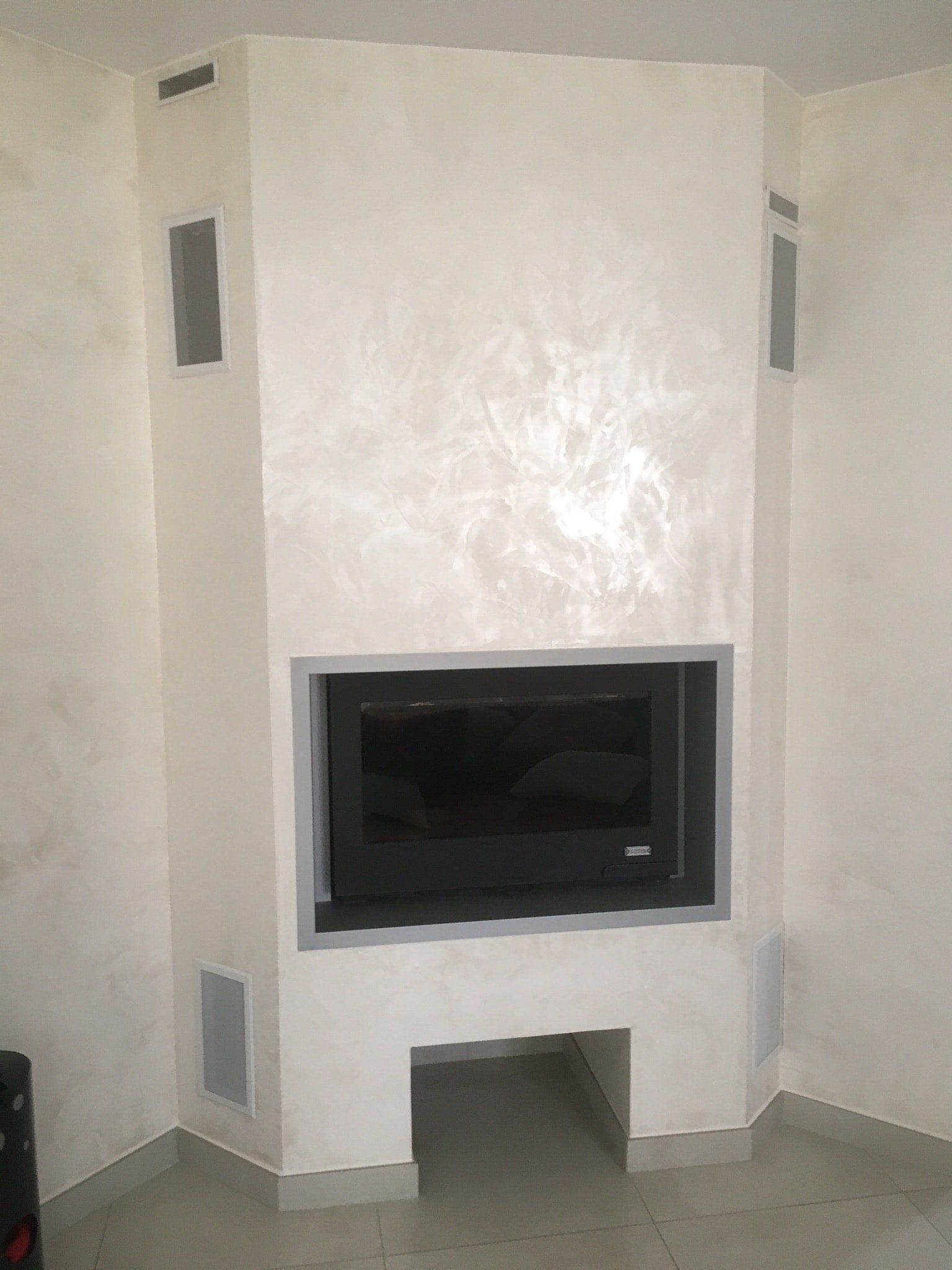 Cheminée d'angle blanche avec pare-étincelles noir, garnitures grises et ouvertures de ventilation.