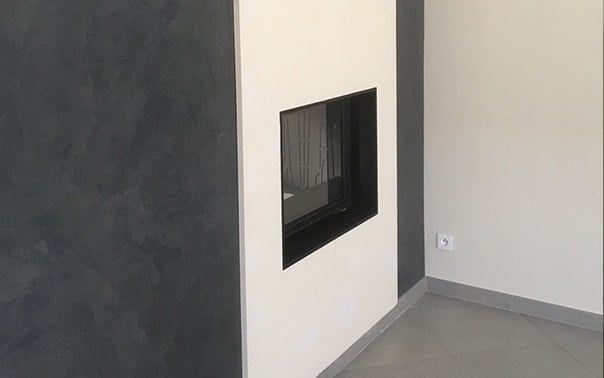 Cheminée moderne encastrée dans un mur blanc, avec un mur texturé gris foncé à gauche.