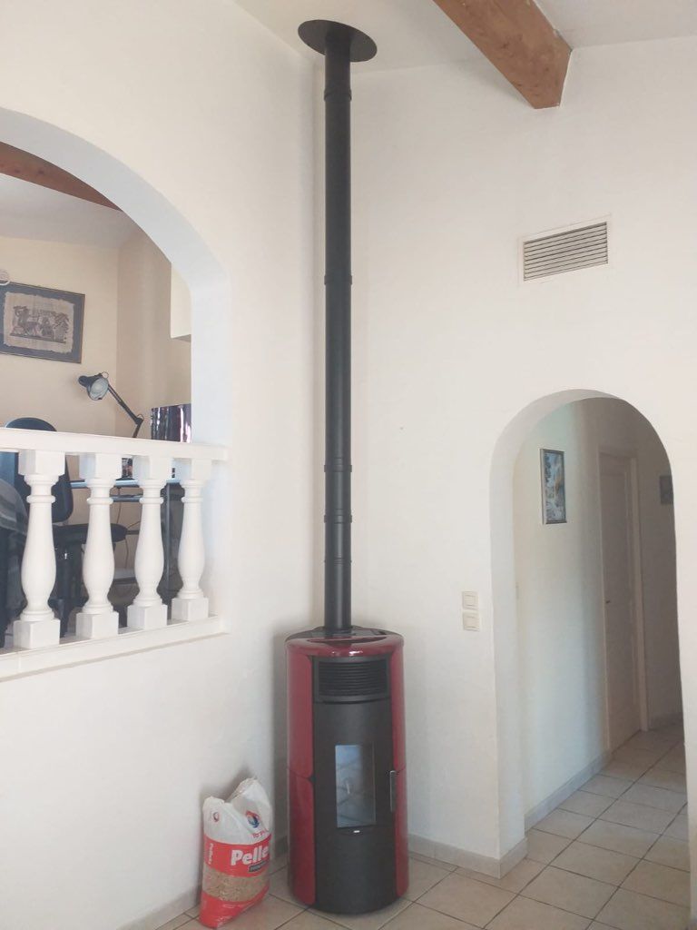 Poêle à granulés rouge et noir avec cheminée noire, murs blancs et porte cintrée.