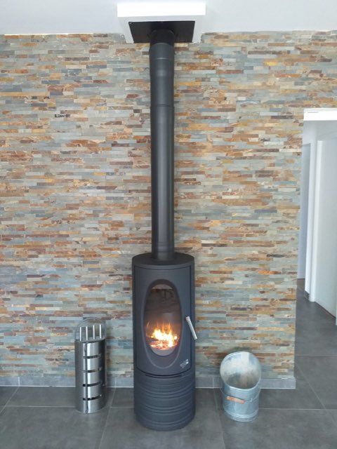 Poêle à bois noir avec un feu allumé contre un mur de pierre, récipient et seau en argent à côté.