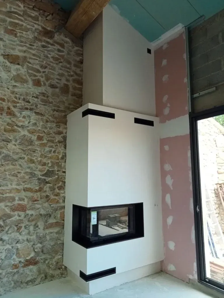 Cheminée blanche avec des accents noirs sur un mur en pierre et des lambris roses.