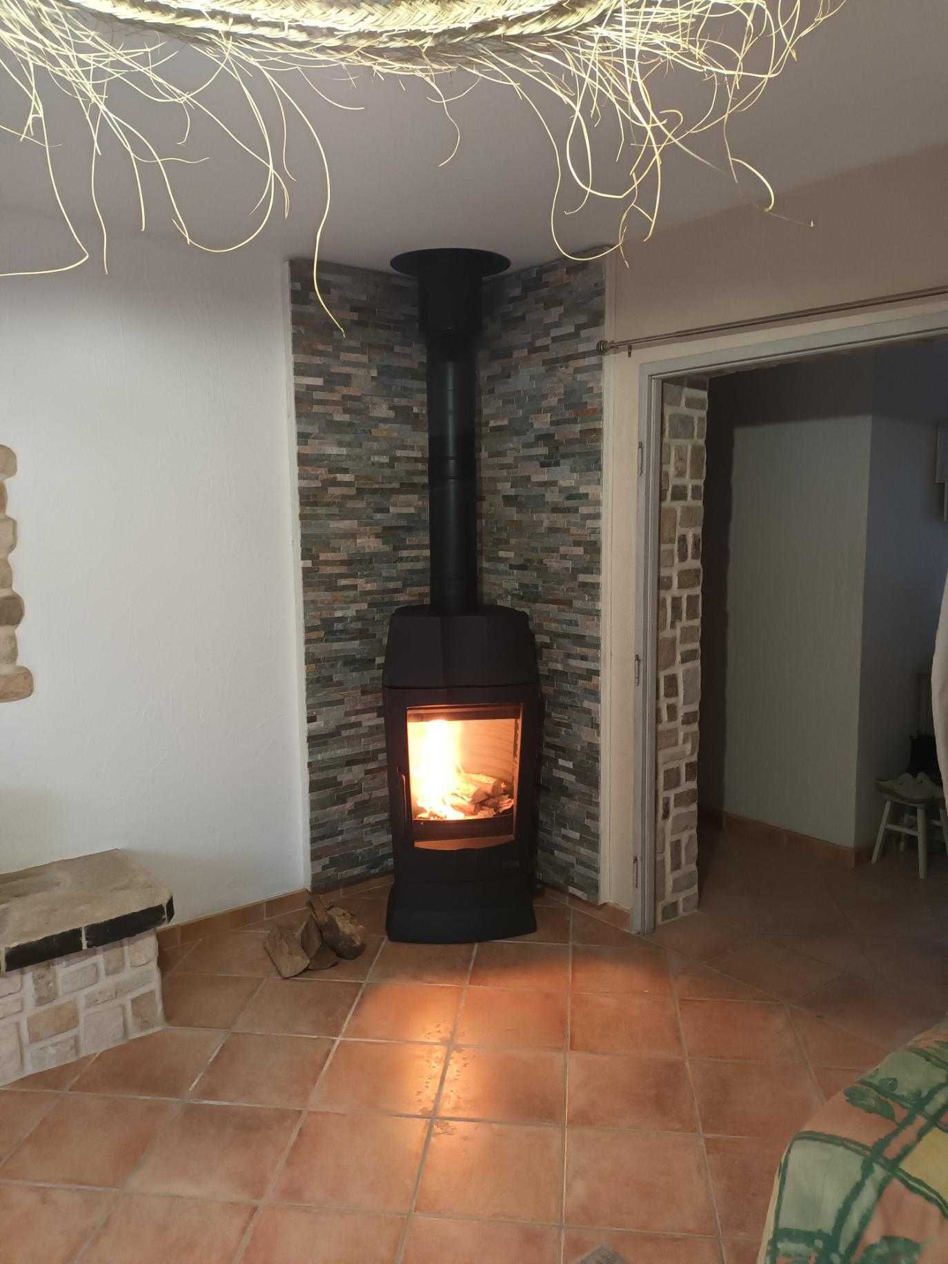 Un poêle à bois avec un feu allumé contre un mur de pierre dans une pièce au sol carrelé.