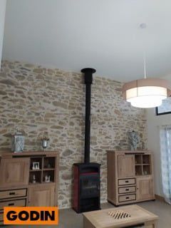 Un poêle à bois avec un conduit de cheminée noir, flanqué d'armoires en bois, contre un mur en pierre.
