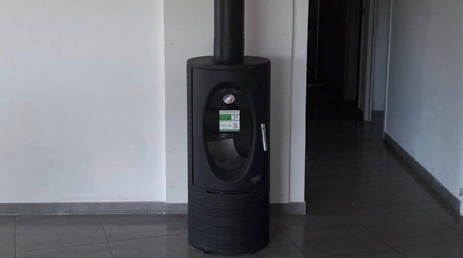 Poêle à granulés noir avec affichage numérique et conduit de cheminée, contre un mur blanc dans un couloir.