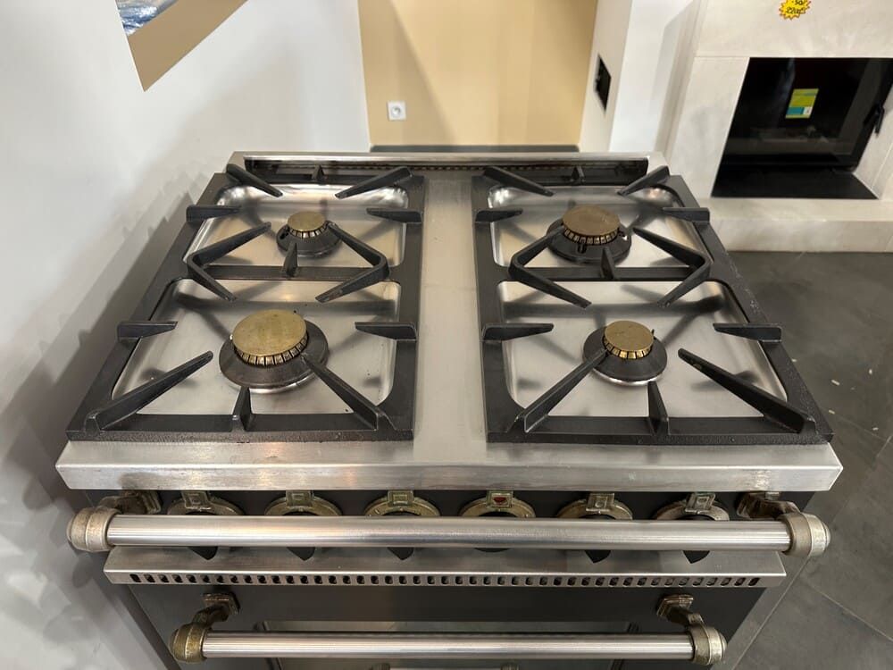 Dans la cuisine, on trouve une cuisinière à bois en acier inoxydable à quatre brûleurs et grilles noires.