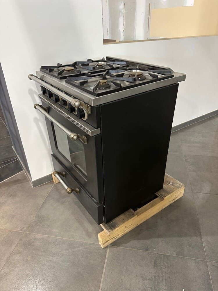 Cuisinière à bois noire sur palette, garniture en acier inoxydable, quatre brûleurs, four avec porte vitrée.