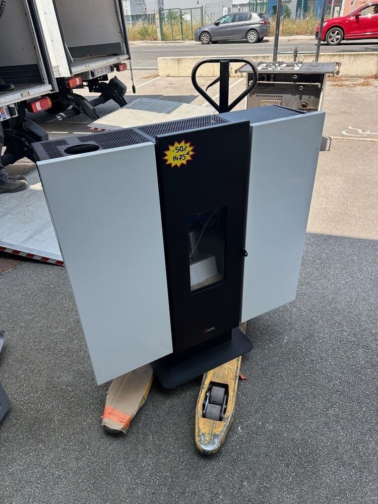 Un poêle à granulés sur un transpalette près d'un camion ; argenté et noir avec un autocollant jaune.