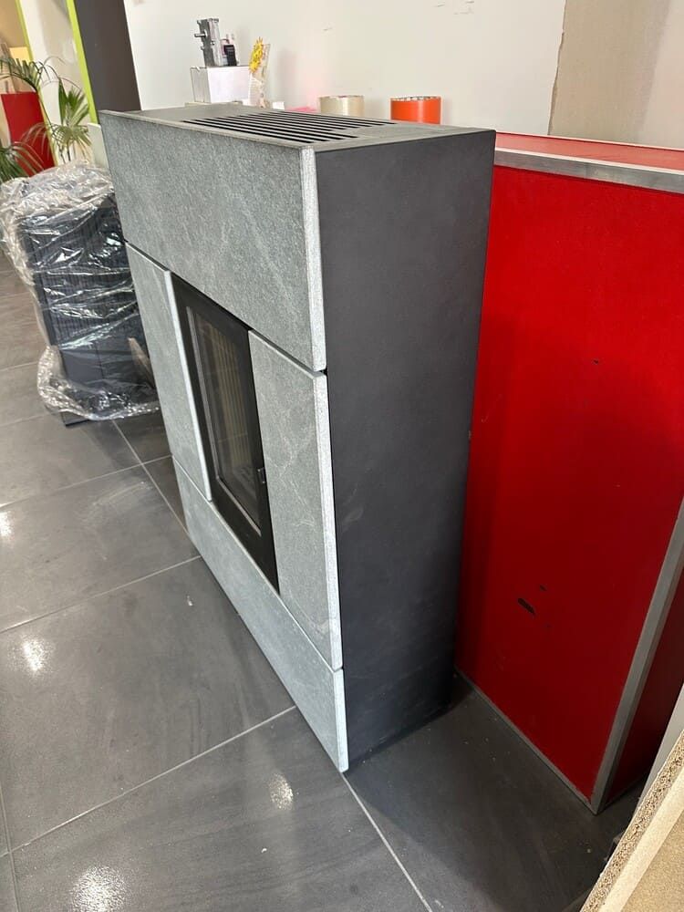 Cheminée grise et noire avec façade en verre, à côté d'un panneau rouge.