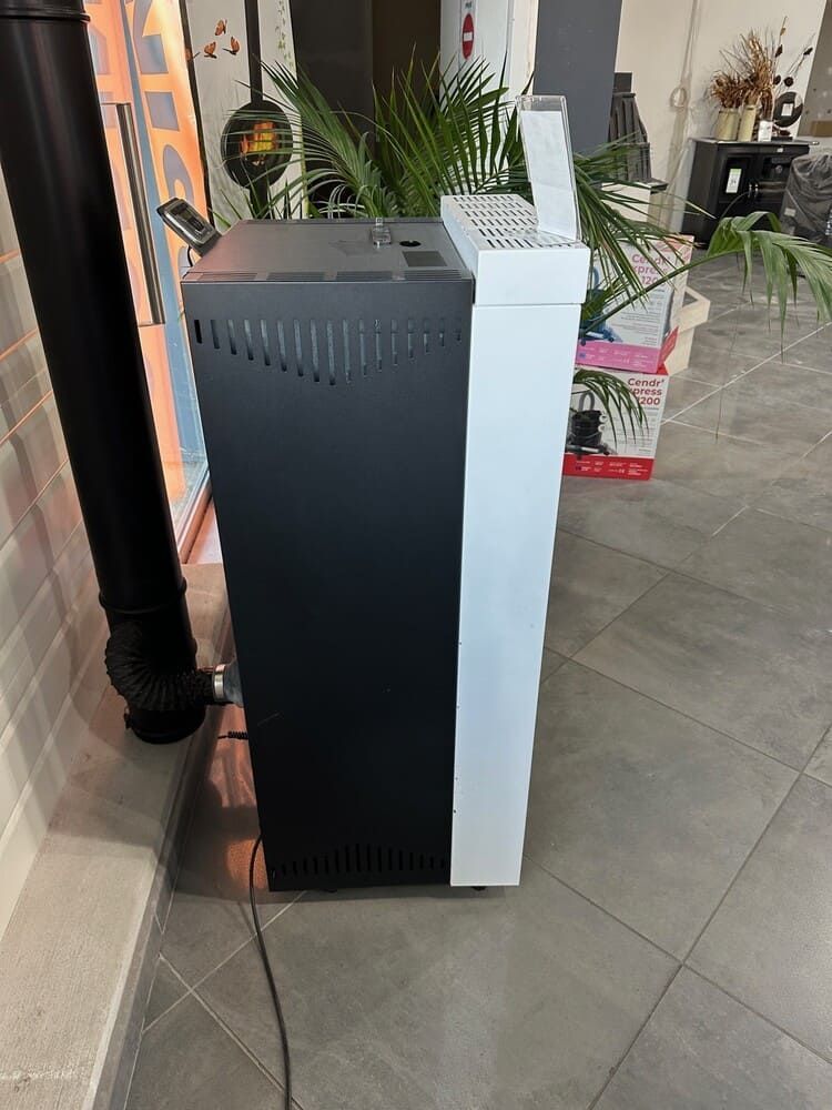 Poêle à granulés noir et blanc avec système d'évacuation et panneau de commande, installé à l'intérieur sur un sol carrelé.