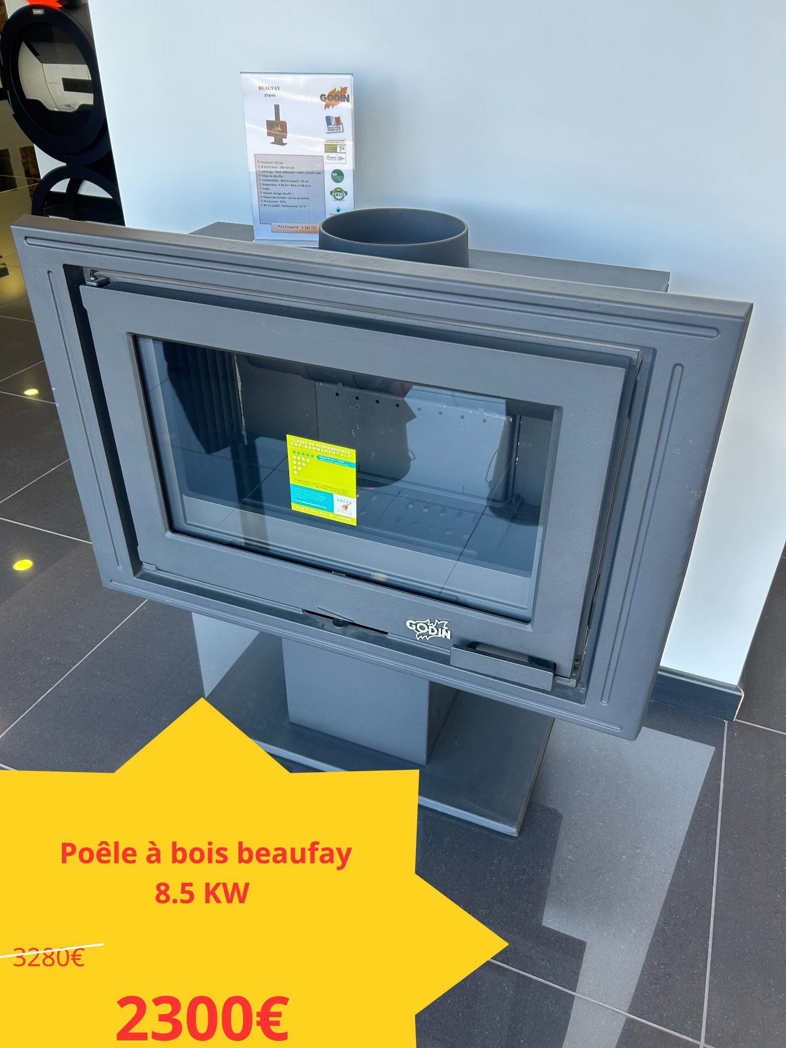 Poêle à bois gris sur piédestal, avec porte vitrée. Étiquette de prix jaune : 2 300 €.