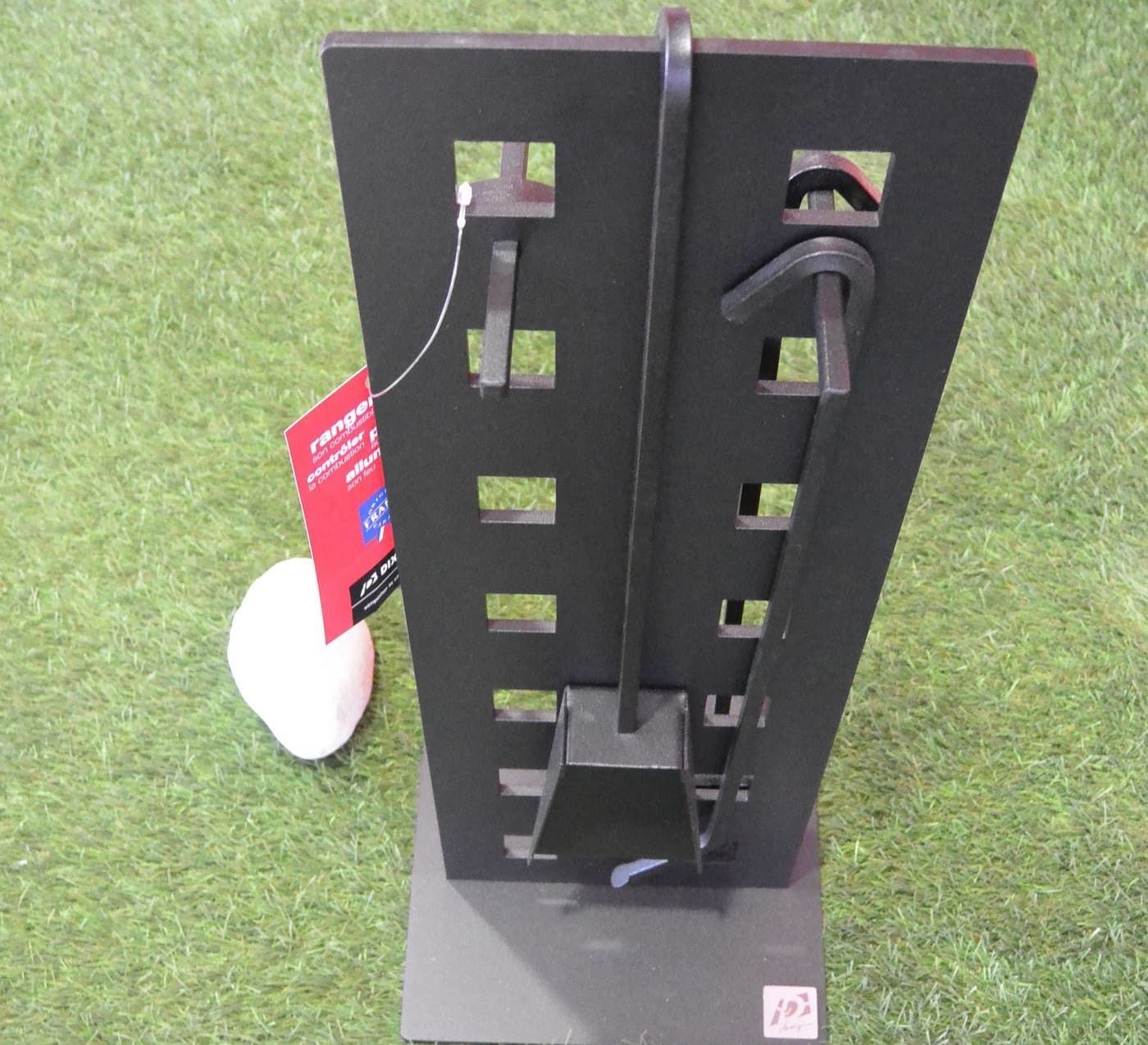 Ensemble d'accessoires de cheminée noirs avec découpes carrées, étiquette rouge, objet blanc sur gazon vert.