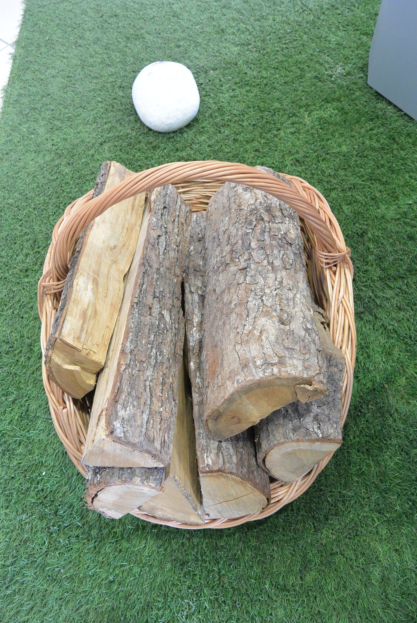 Panier rempli de bois de chauffage sur du gazon artificiel vert ; une boule blanche au-dessus.