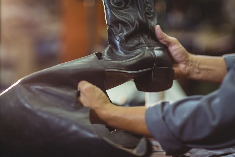 Una persona sostiene un par de botas de vaquero en sus manos.