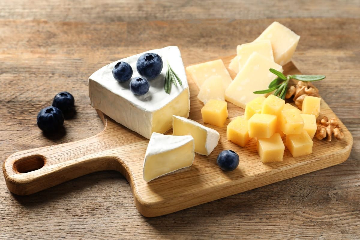 Una tabla de cortar de madera cubierta con diferentes tipos de queso y arándanos.