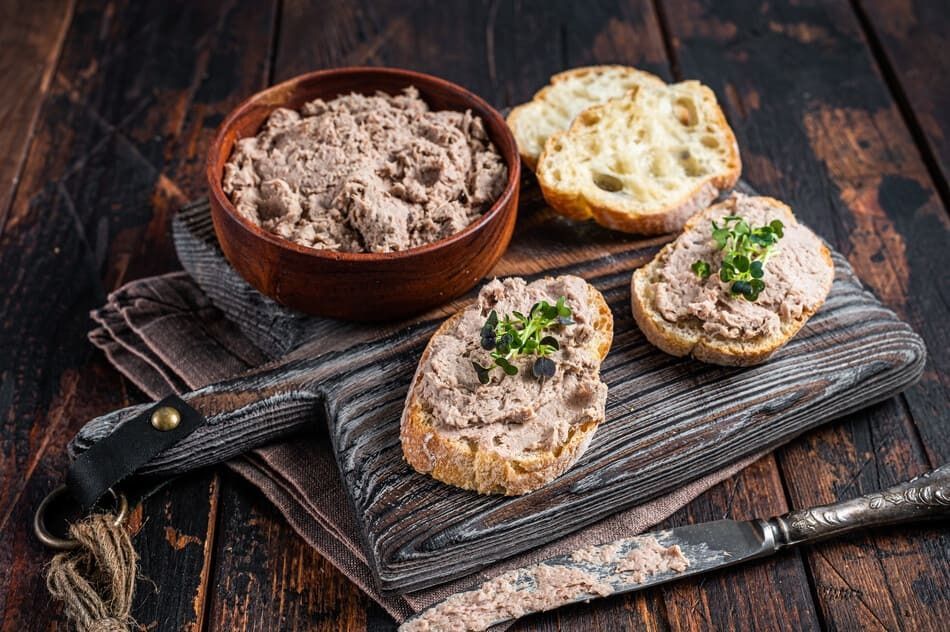 Una tabla de cortar de madera cubierta con rebanadas de pan y un tazón de paté.