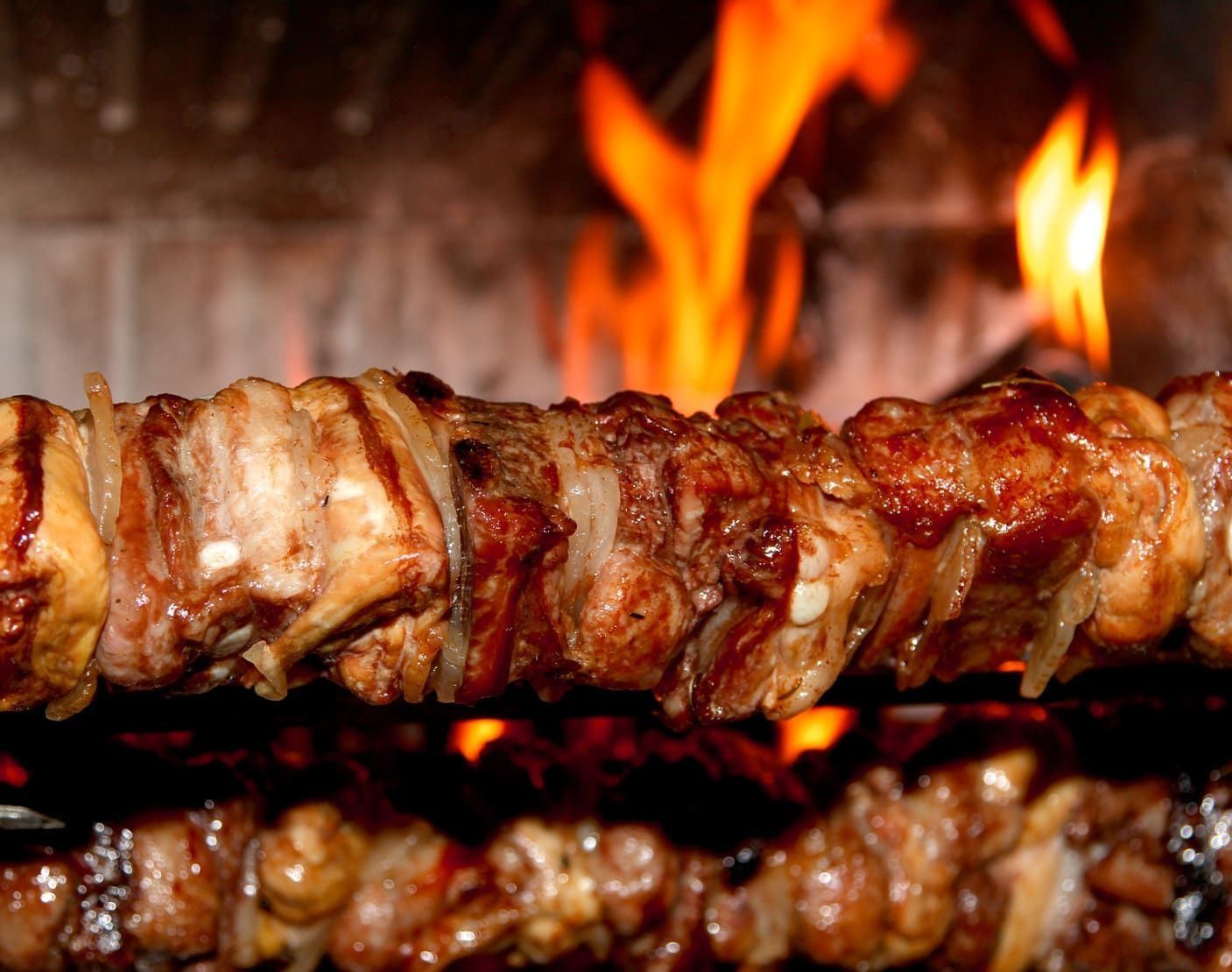 Un trozo de carne se está cocinando en una parrilla frente a un fuego.
