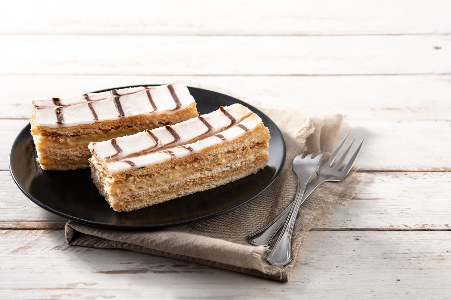 Dos rebanadas de pastel en un plato negro con un tenedor.