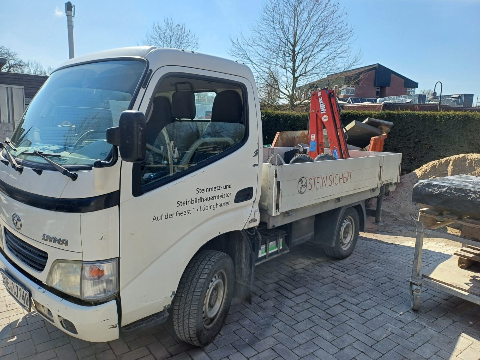 Ein weißer Lastwagen mit einem Kran auf der Ladefläche steht auf einer gepflasterten Auffahrt.
