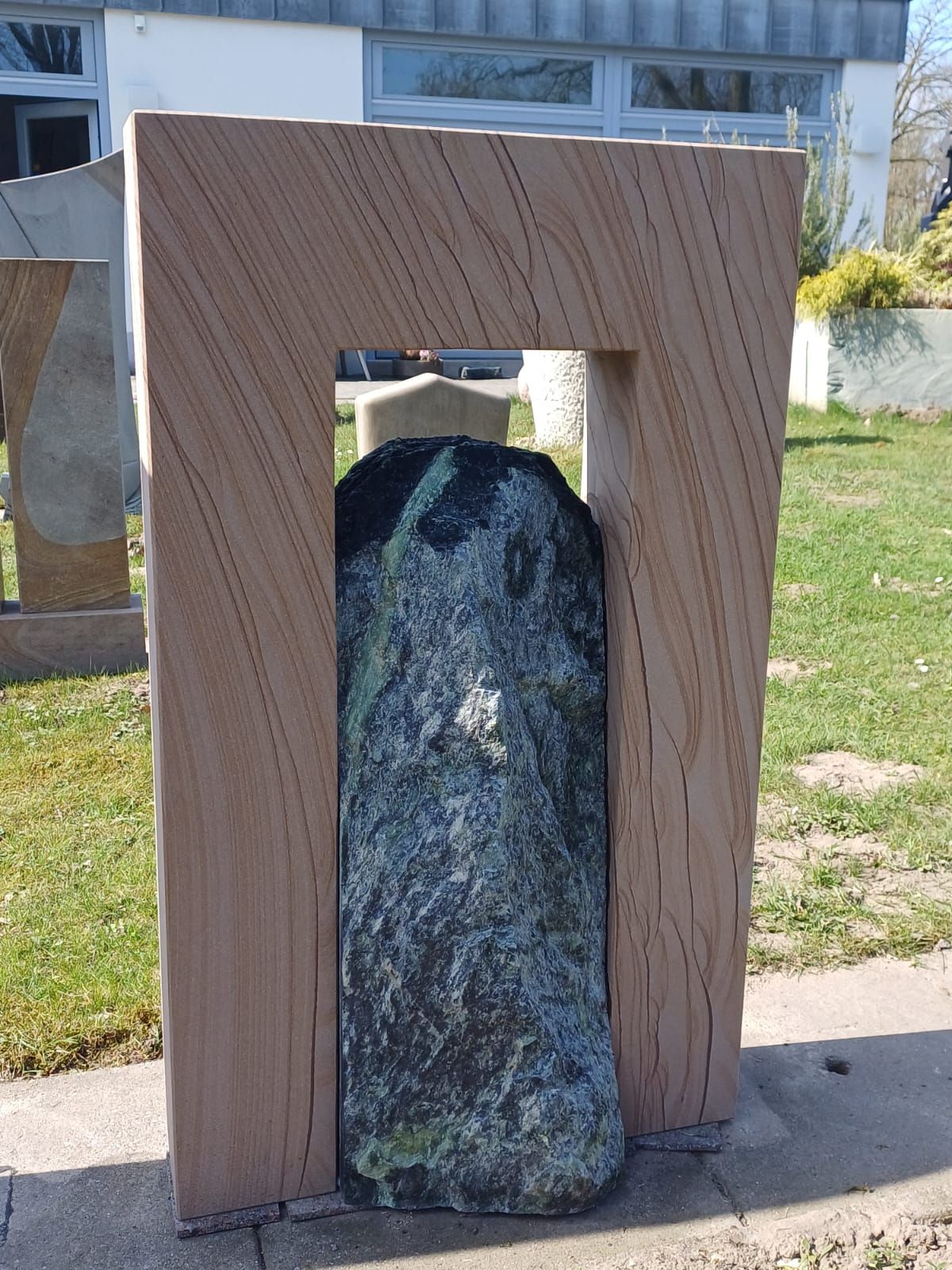 Eine große Steinskulptur steht im Gras vor einem Gebäude.