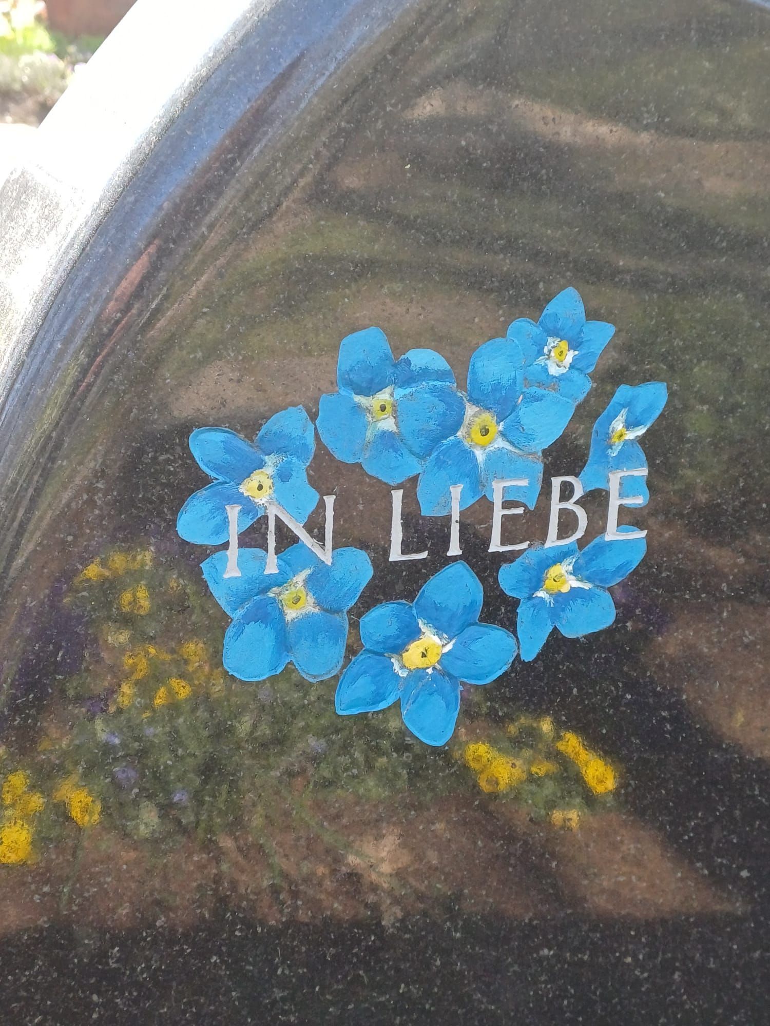 Malerei auf einem Grabstein mit blauen Blumen und den Worten „in Liebe“ darauf