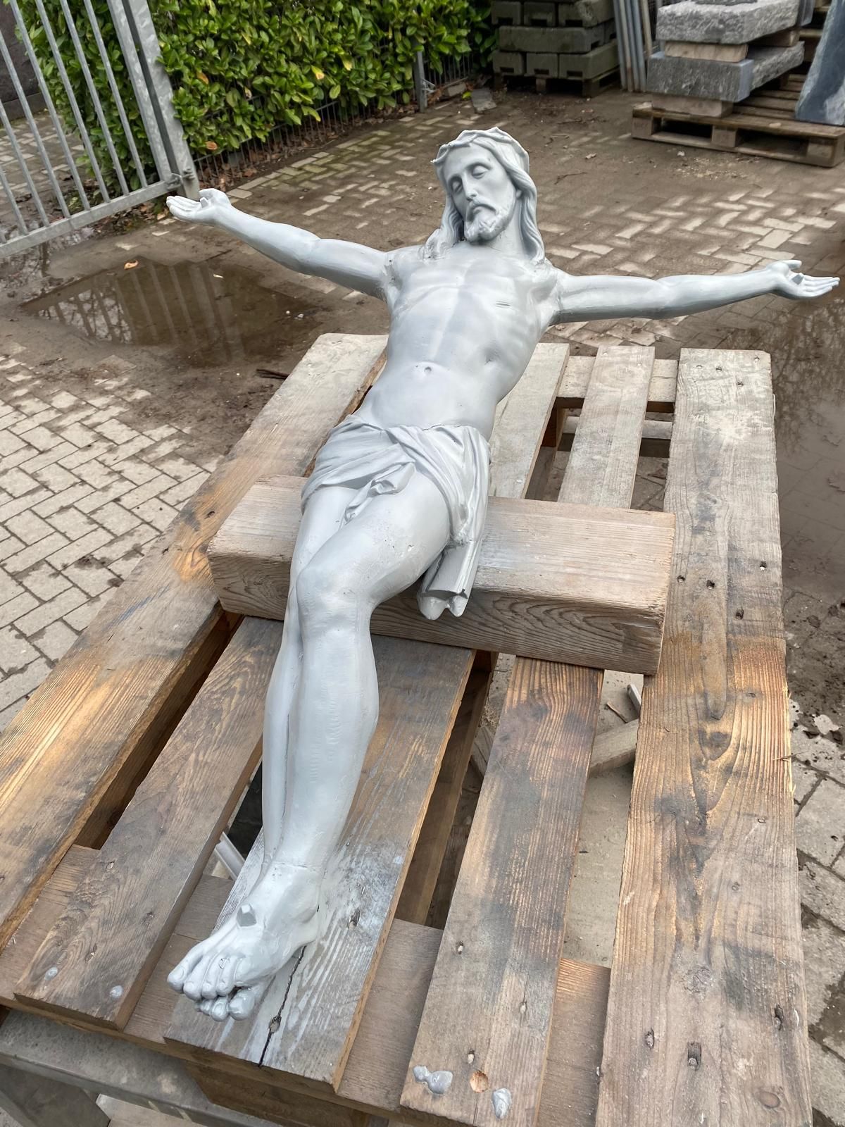 Auf einer Holzpalette sitzt eine Statue von Jesus am Kreuz.