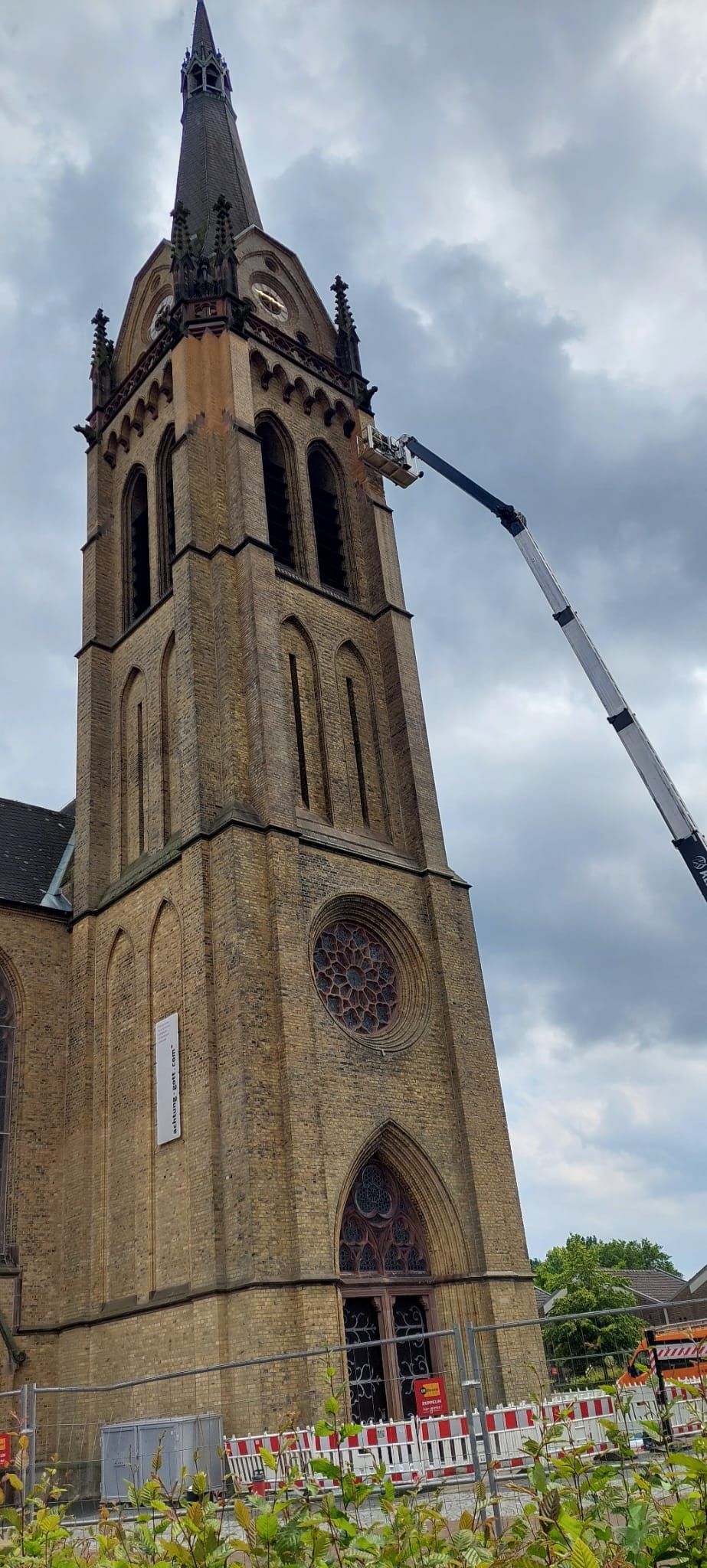 Ein großer Backsteinkirchturm wird von einem Kran gereinigt.