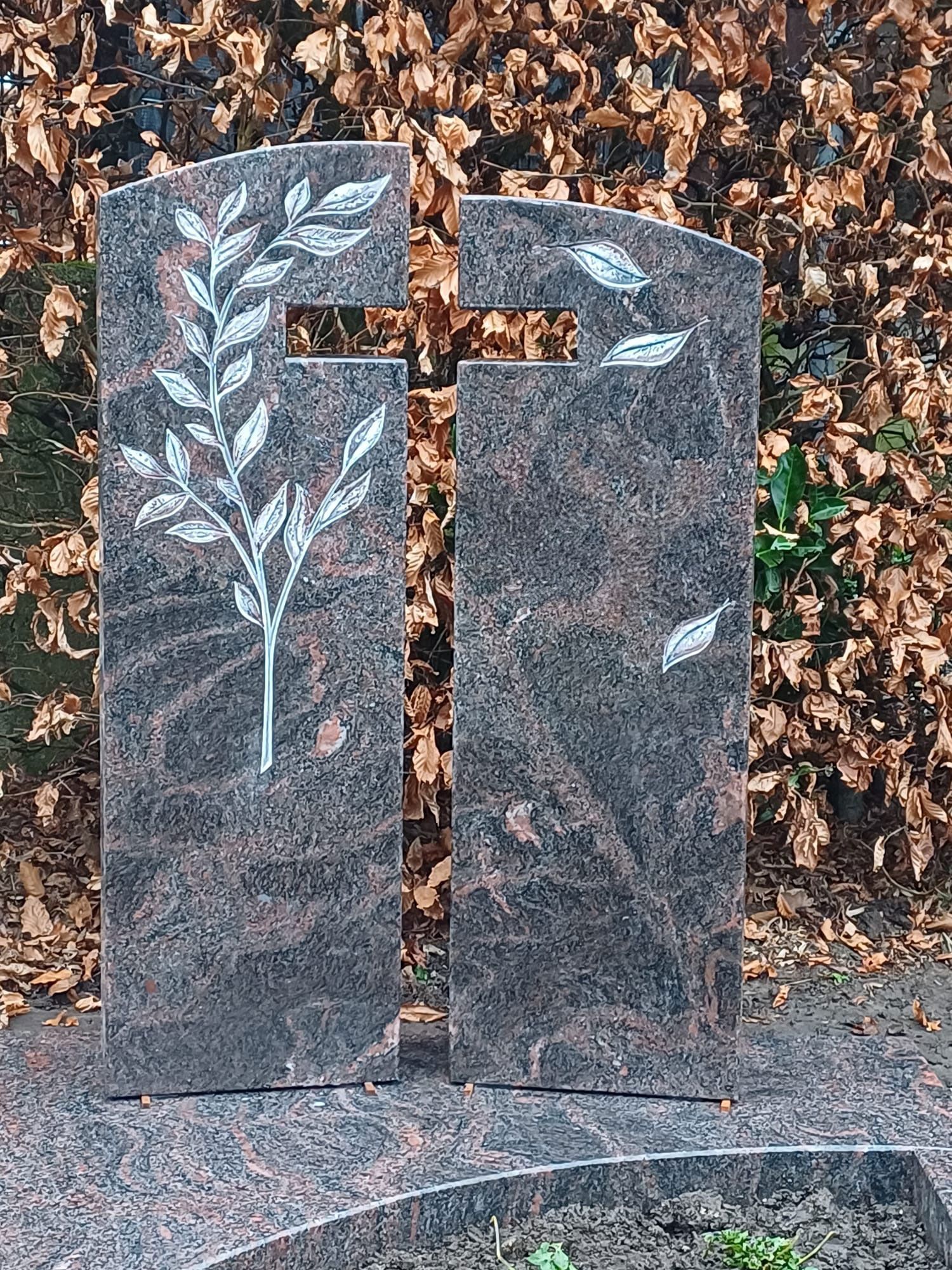 Ein Grabstein mit einem Kreuz und Blättern darauf.