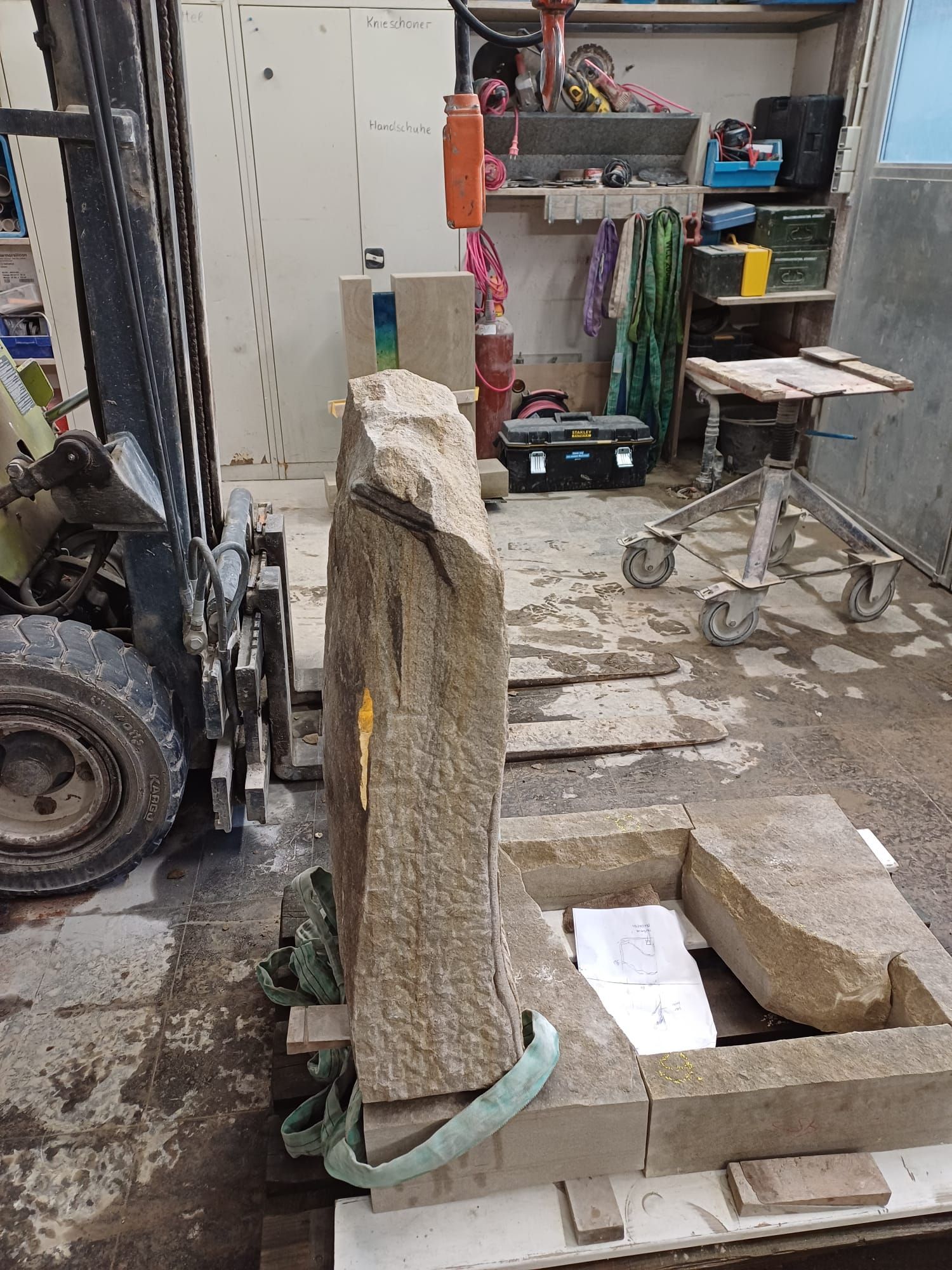 Ein Gabelstapler bewegt einen großen Stein in einer Werkstatt.