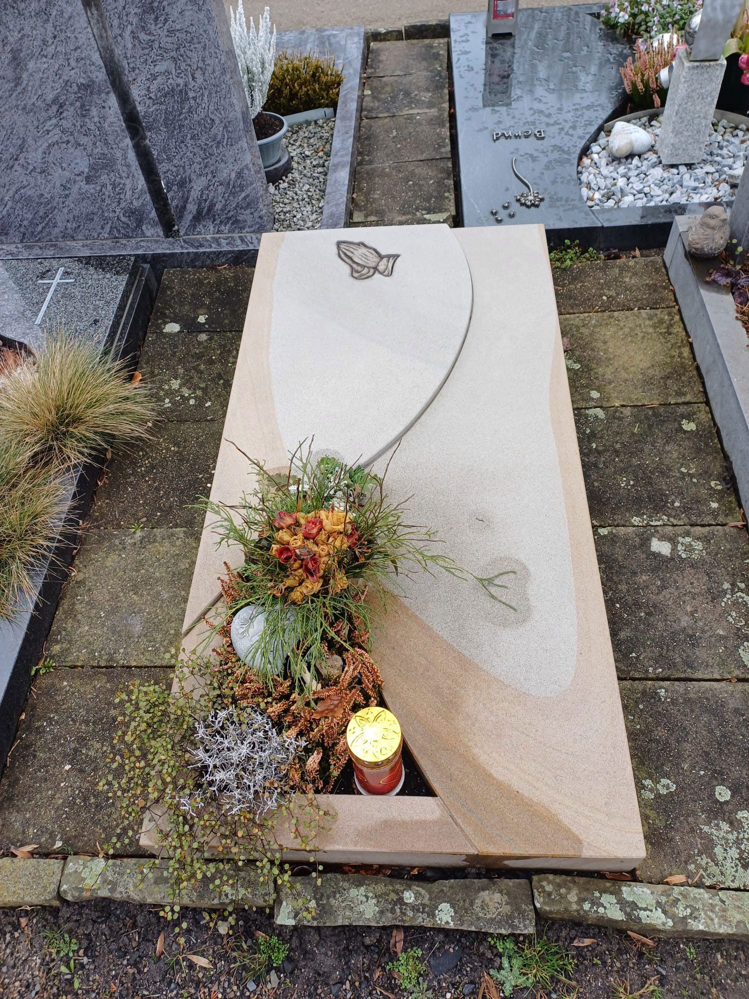 Ein Grab mit Blumen und einer Kerze darin auf einem Friedhof.