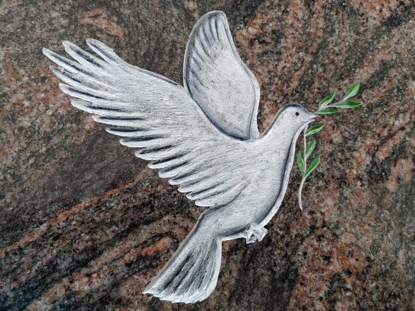 Eine Statue einer fliegenden Taube mit einem Zweig im Schnabel.