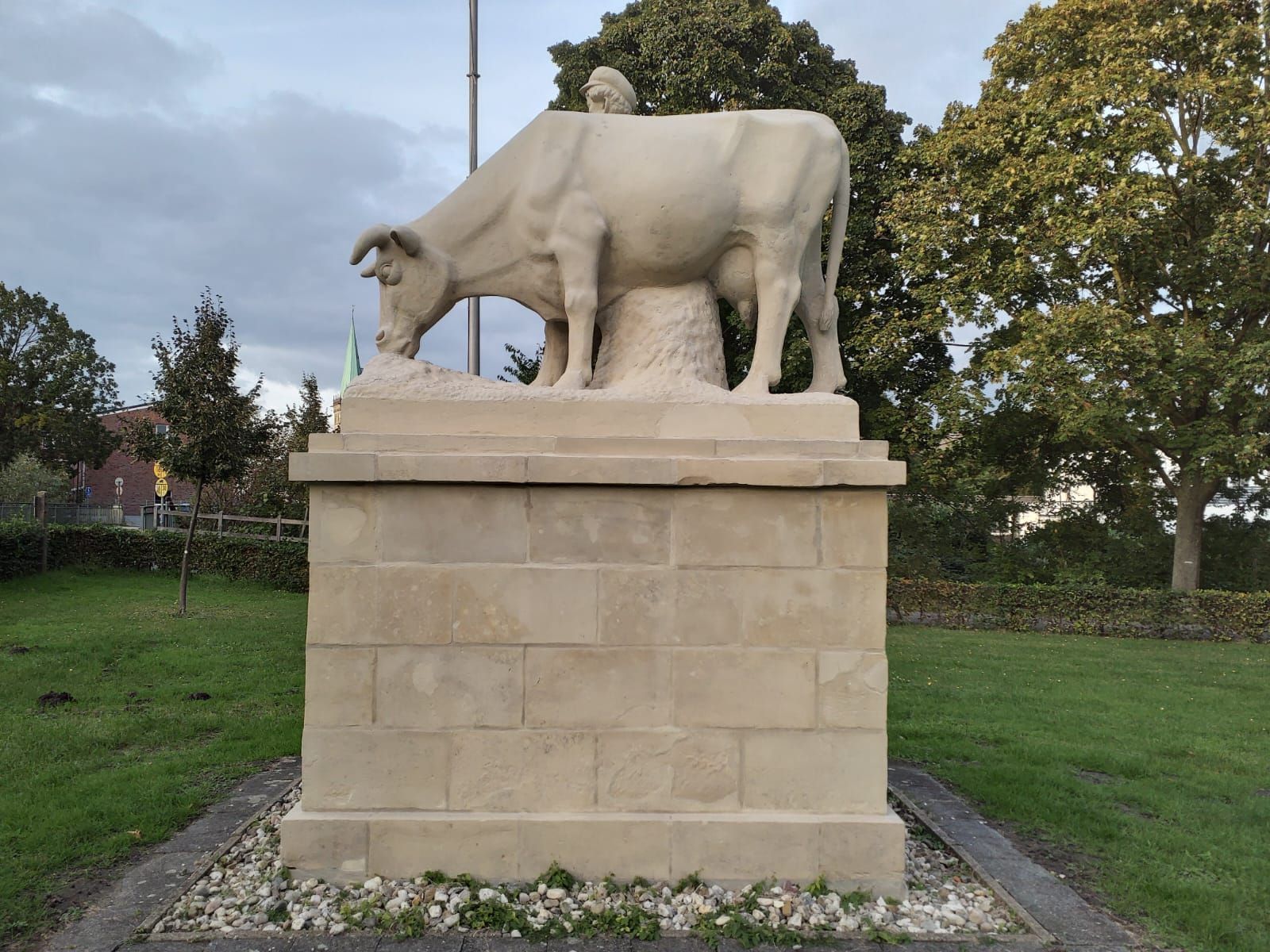Eine Statue einer Kuh auf einem Sockel in einem Park