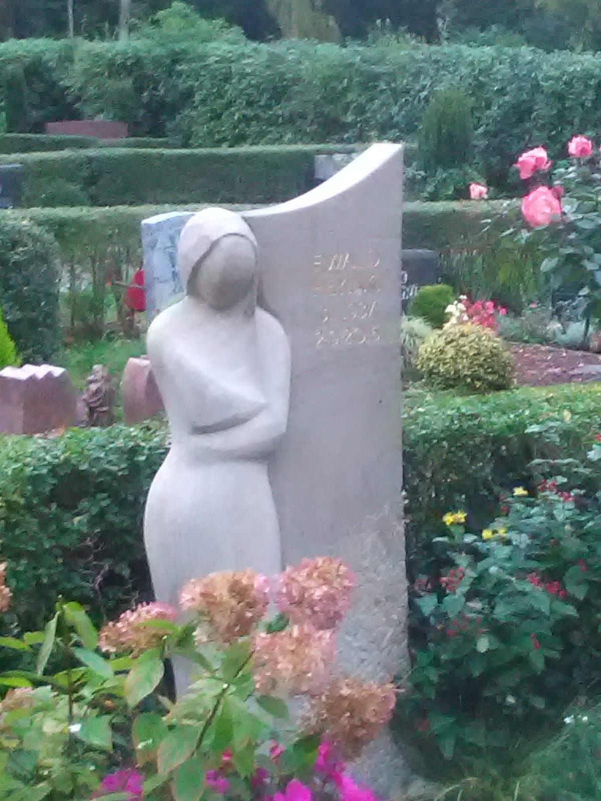 Eine Frauenstatue, die neben einem Grabstein auf einem Friedhof steht.