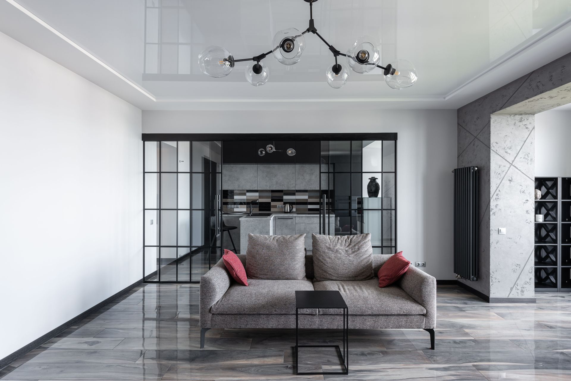 Sala de estar moderna con sofá gris, mampara de cristal, suelo de mármol y lámpara de araña negra.