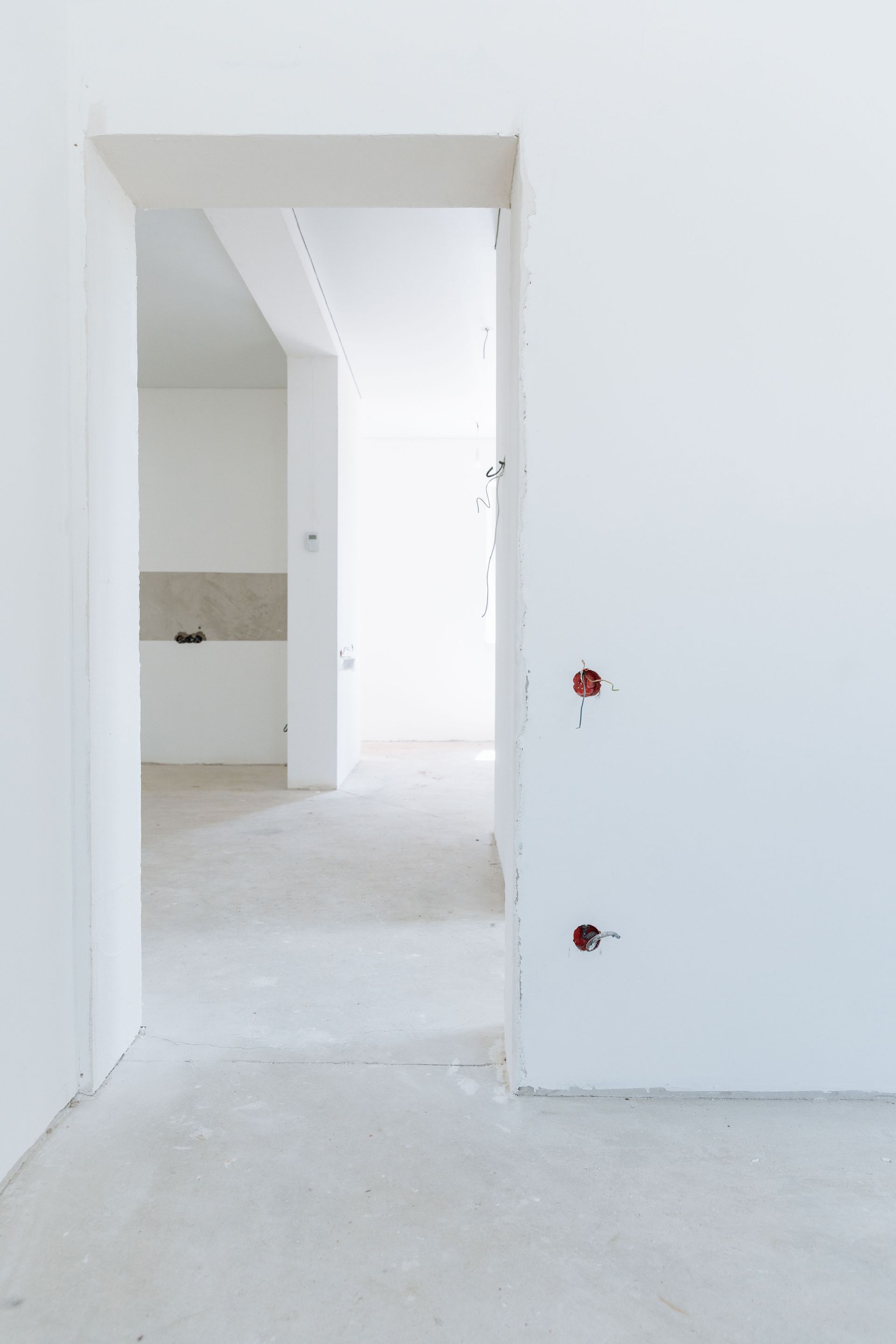 Pasillo y puerta de entrada blancos sin terminar en una habitación vacía con enchufes de pared a la vista.