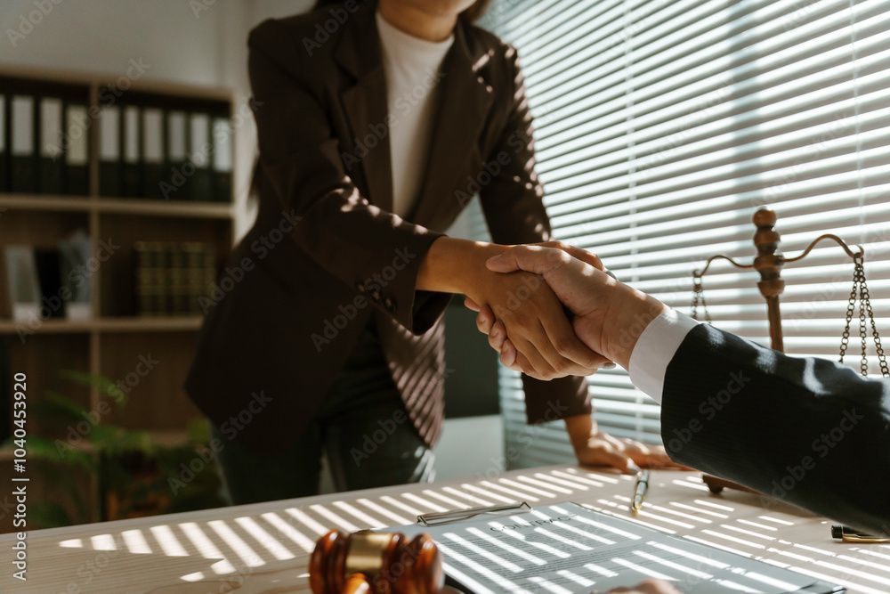 Due persone in giacca e cravatta si stringono la mano in un ufficio, con una bilancia della giustizia sul tavolo.