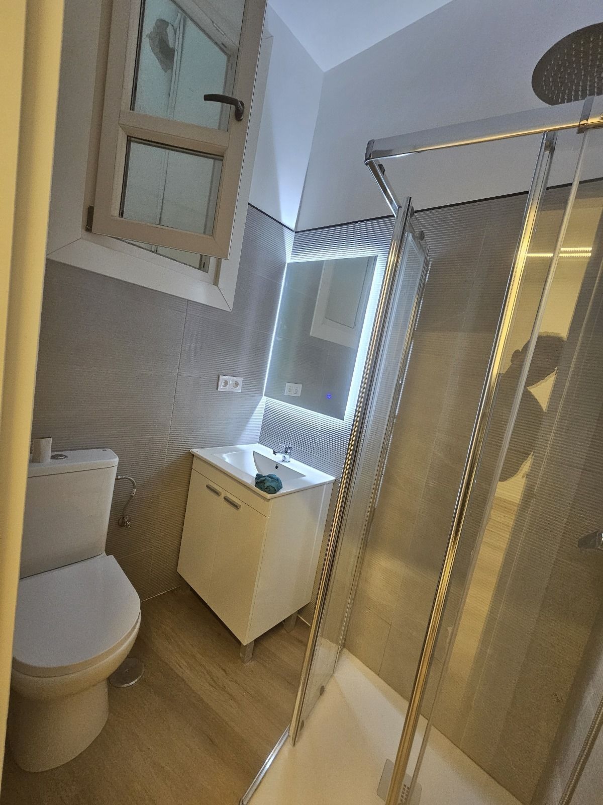 Baño pequeño con inodoro, lavabo y ducha de cristal. Colores beige y blanco.
