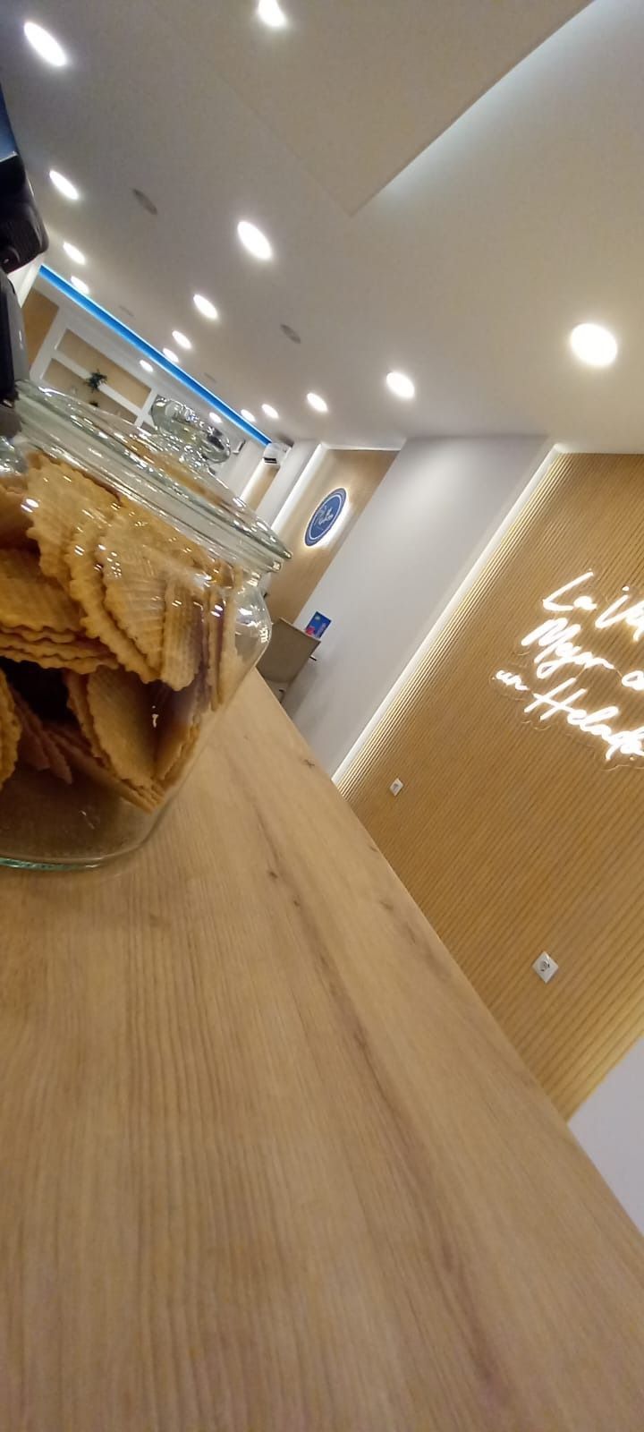Mesa de madera con un tarro de galletas, pared color crema con un letrero de neón y luces de techo.