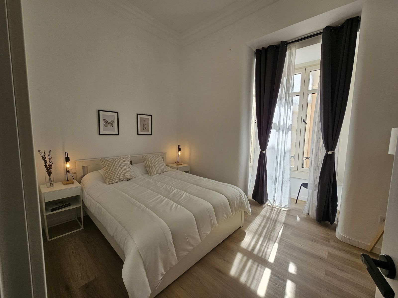 Dormitorio con cama, mesitas de noche, ventana con cortinas y obras de arte decorativas.