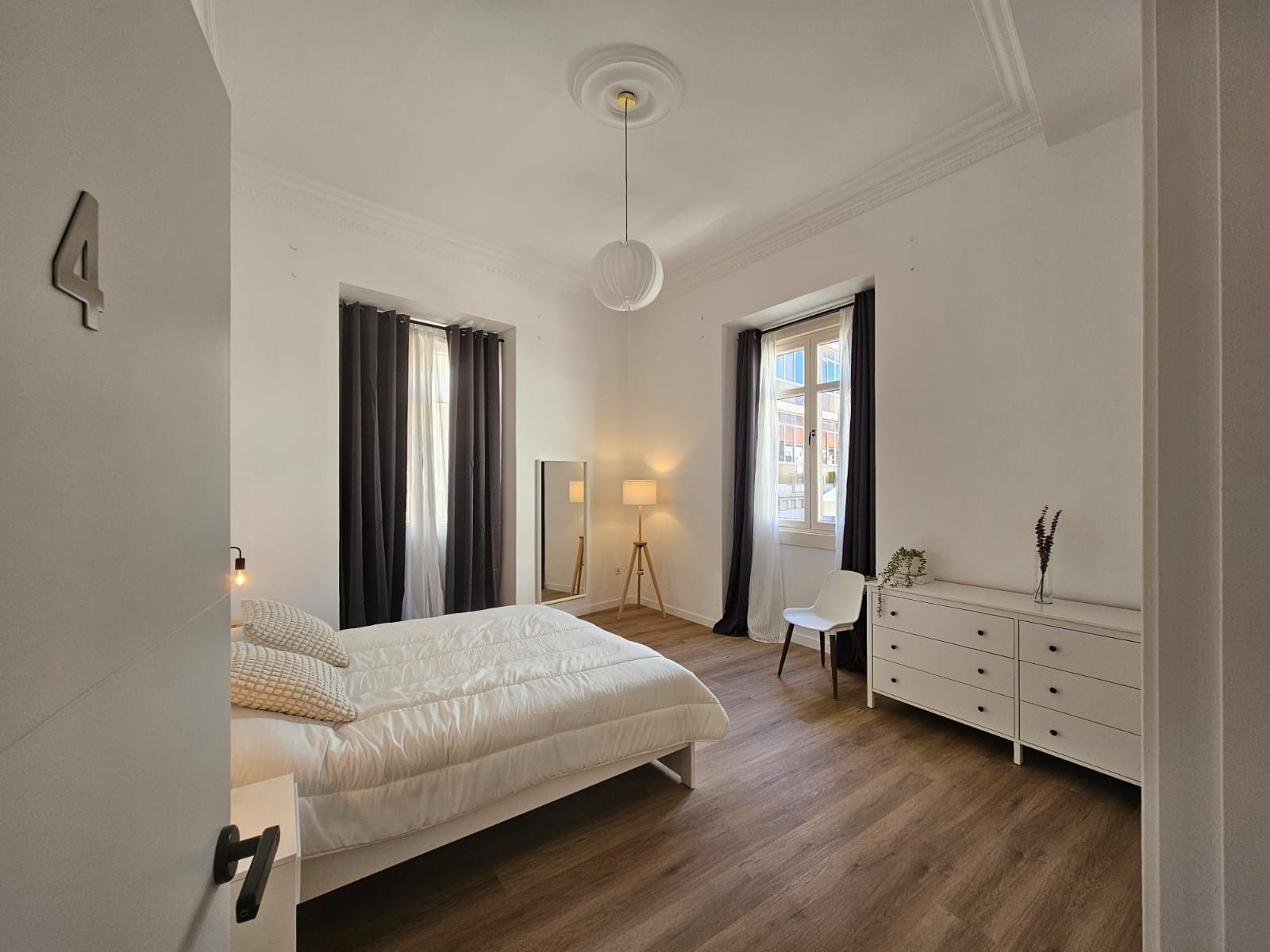 Interior de dormitorio con cama, tocador, ventana y lámpara colgante.