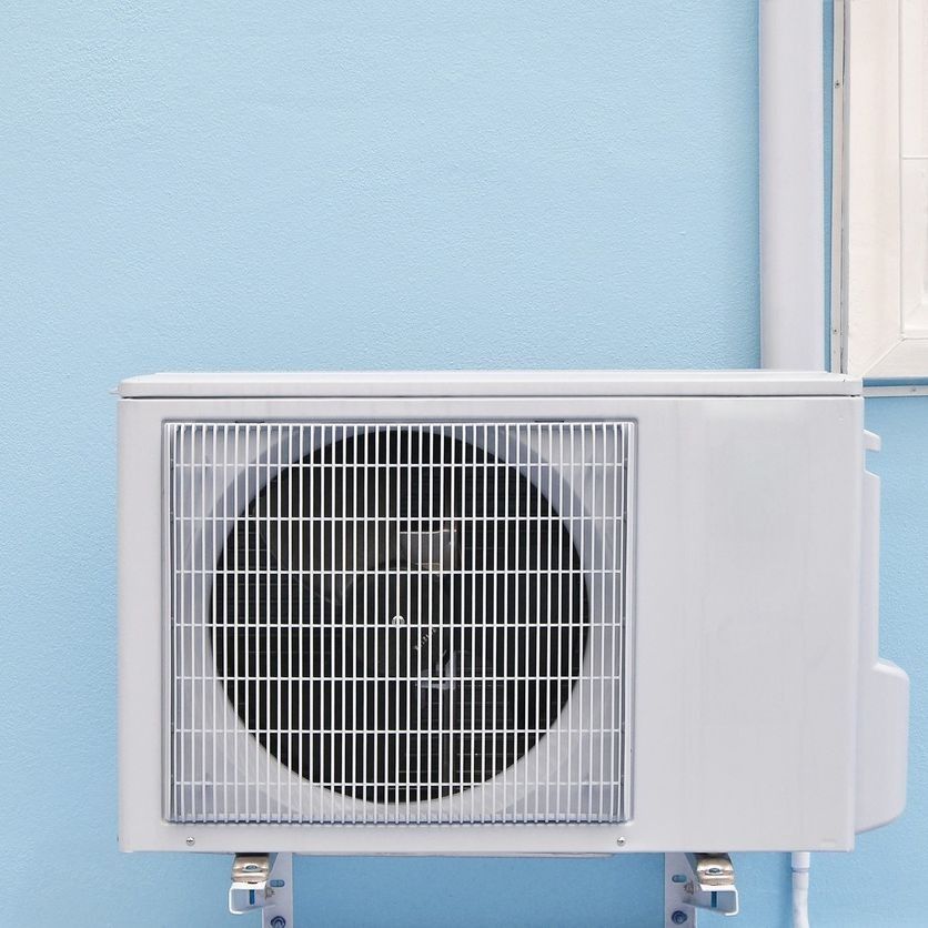 Unidad de aire acondicionado blanca montada en una pared azul claro.