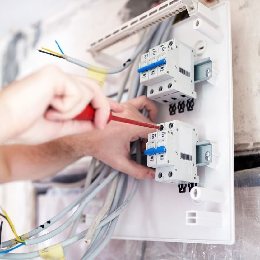 Electricista instalando disyuntores en un panel blanco; cableado visible.