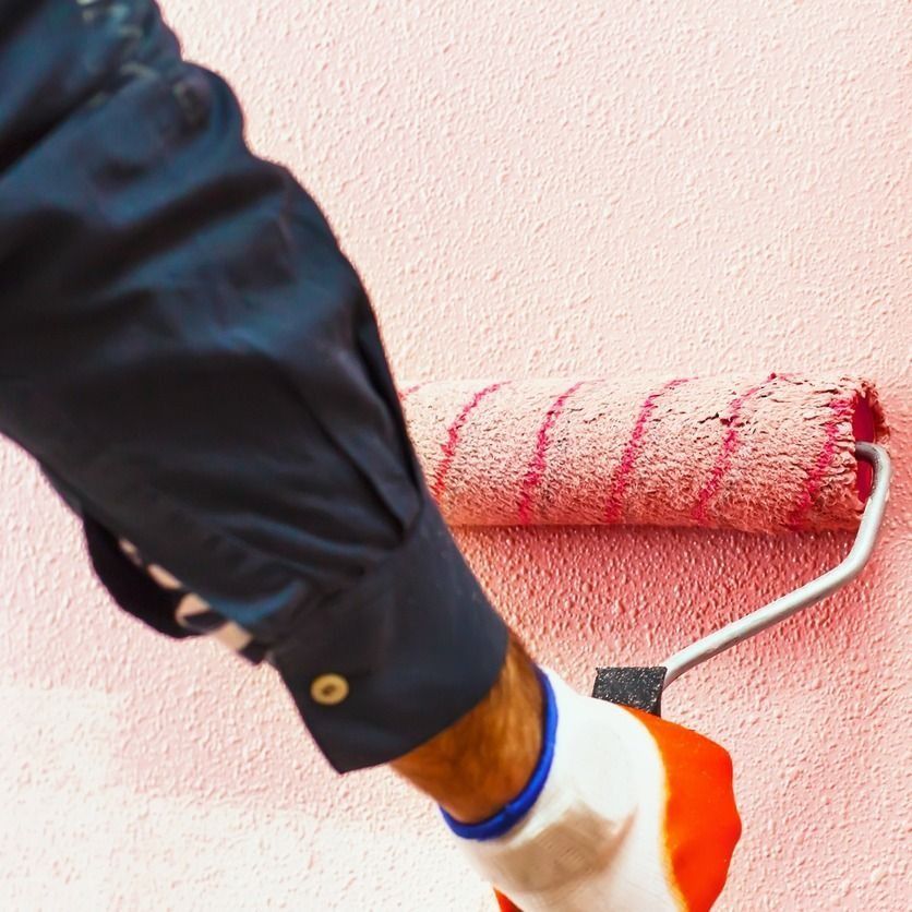 Persona con guante pintando una pared texturizada de color rosa con un rodillo de pintura.