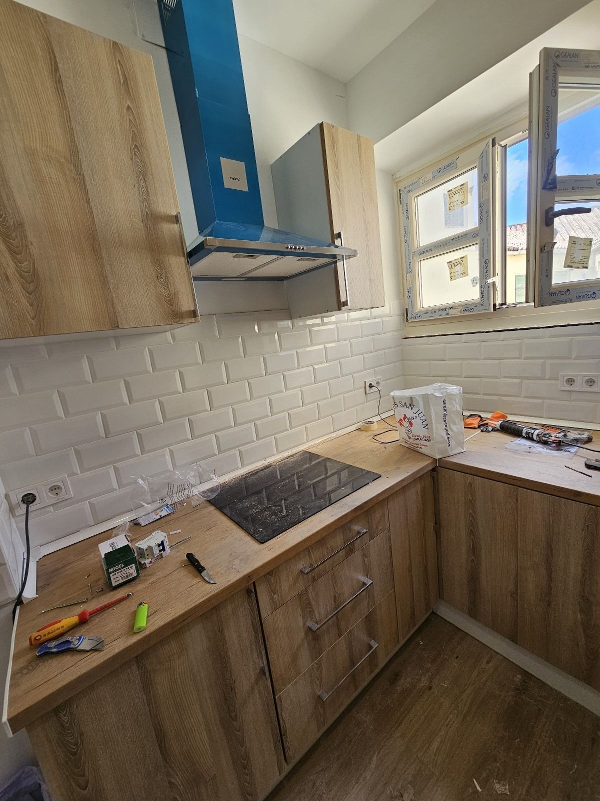 Una cocina en construcción con gabinetes de madera, salpicadero de azulejos de ladrillo blanco y una campana extractora azul.