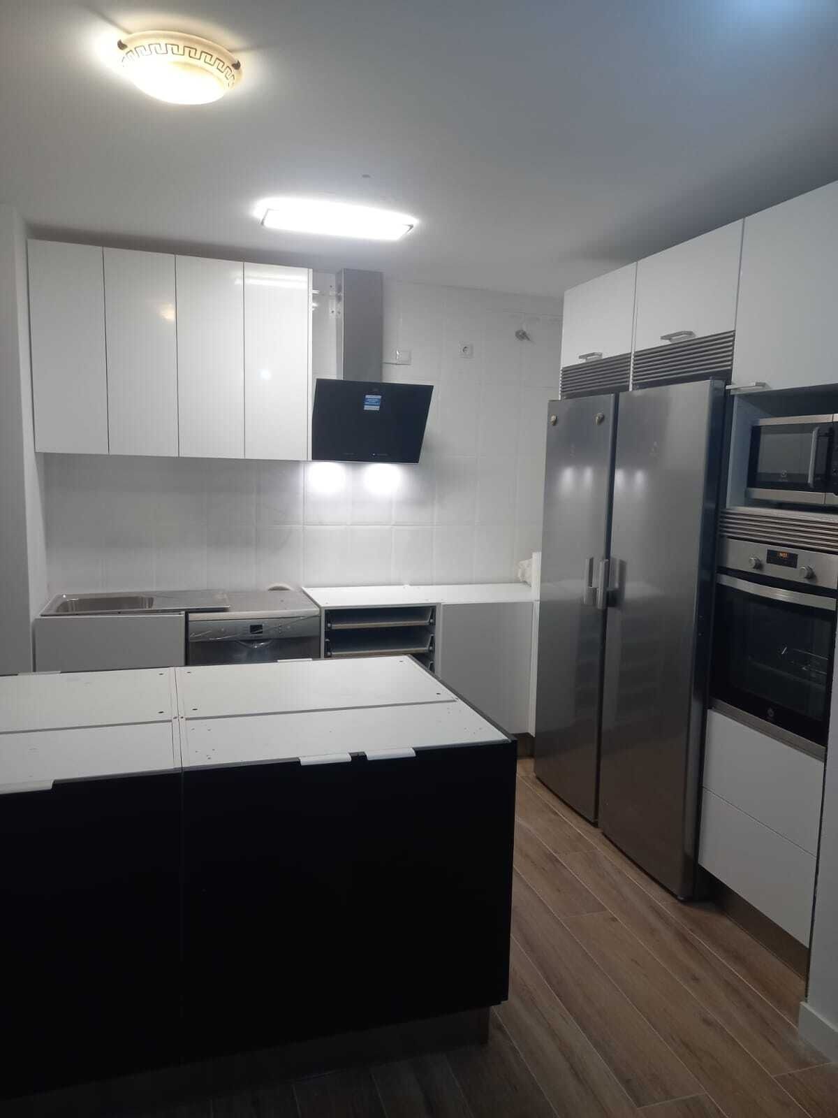 Cocina blanca moderna con isla oscura, electrodomésticos de acero inoxidable y pisos con apariencia de madera.