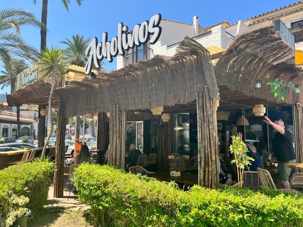 Un restaurante llamado "Rabelinos" con techo de paja, con asientos al aire libre; día soleado.