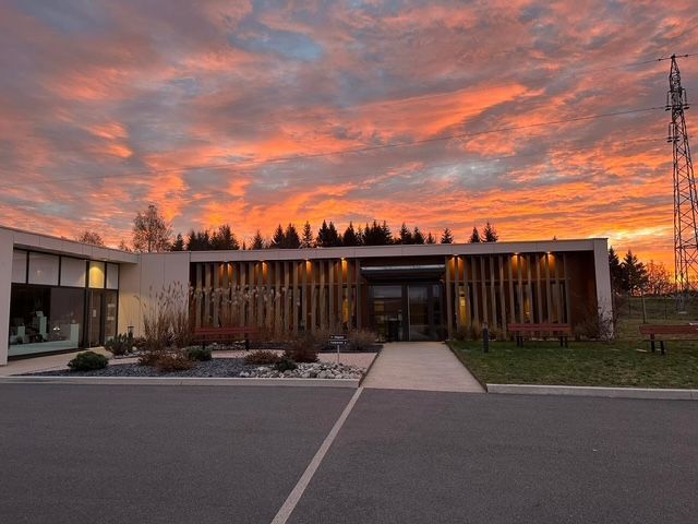 Bâtiment bas moderne au coucher du soleil, avec un ciel orange spectaculaire et une allée piétonne à l'avant.