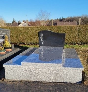Monument funéraire en granit avec une pierre tombale noire polie dans un jardin de cimetière ensoleillé